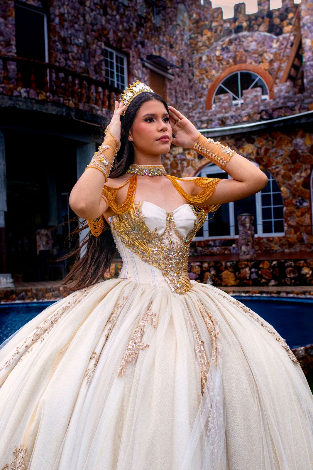 Quinceañera con vestido dorado frente a un castillo de piedra