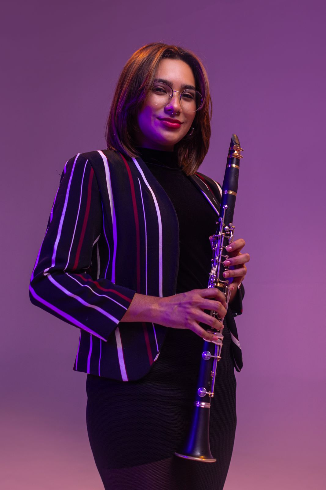 Retrato de estudio de una clarinetista con blazer a rayas y luz morada